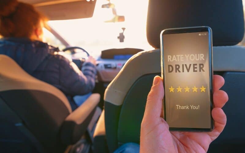 Passenger is sitting on the back seat of the car and using smart phone app to rate a driver. Taxi or modern peer to peer ridesharing concept