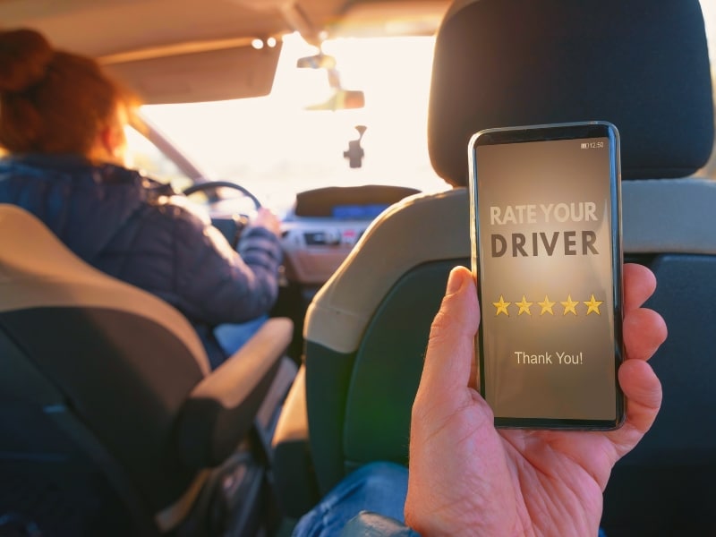 Passenger is sitting on the back seat of the car and using smart phone app to rate a driver. Taxi or modern peer to peer ridesharing concept