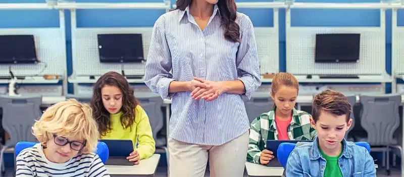 Woman standing watching students working on tablets.