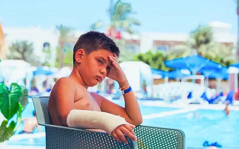 Sad kid with arm cast near swimming pool.
