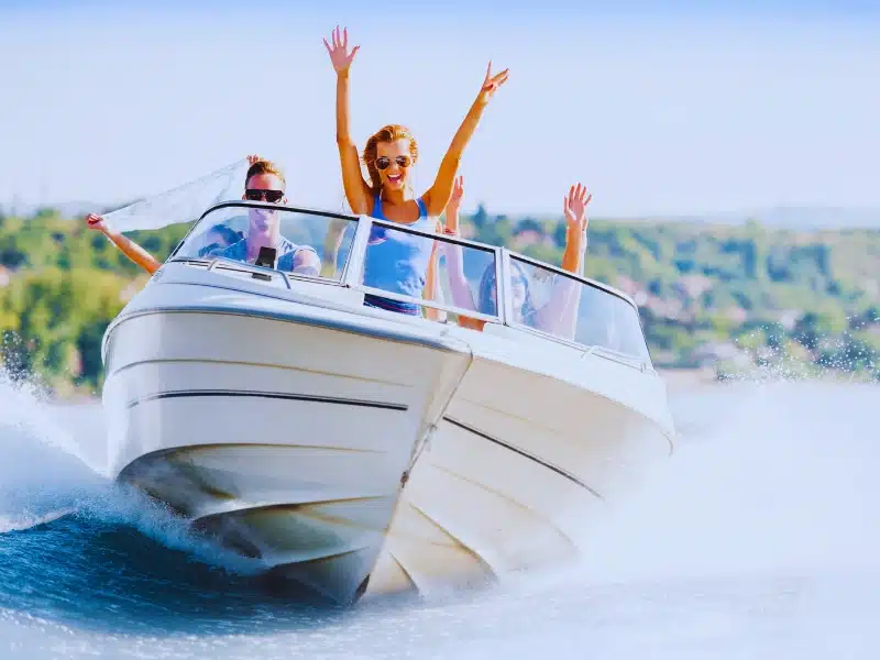 Group of young people with raised hands enjoying in a speedboat ride.