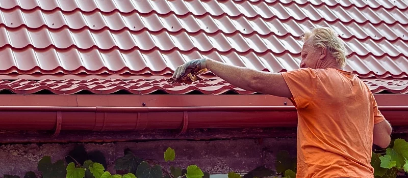 A man cleans out debris and leaves from the gutter system on the roof of his house.