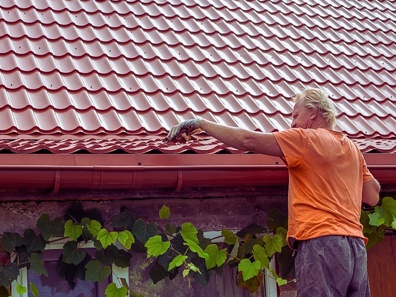 A man cleans out debris and leaves from the gutter system on the roof of his house.