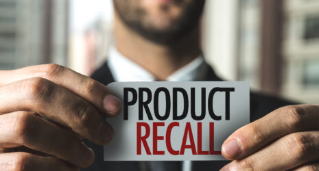 Man in suit holding a piece of paper with Product Recall printed in black and red.