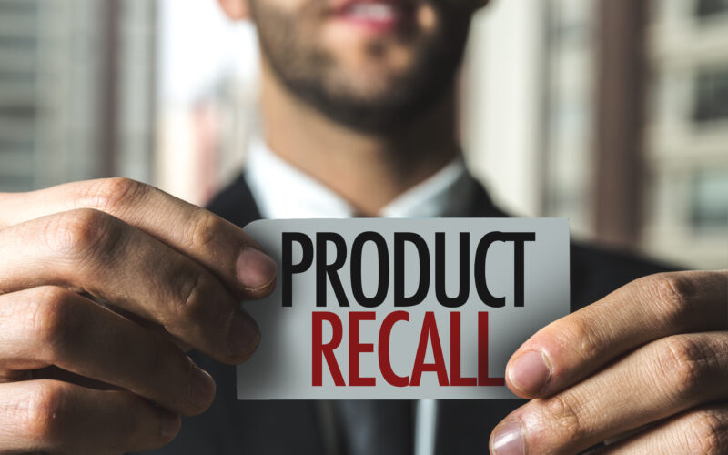 Man in suit holding a piece of paper with Product Recall printed in black and red.
