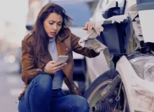 Young sad woman text messaging on smart for after a car crash on the road.