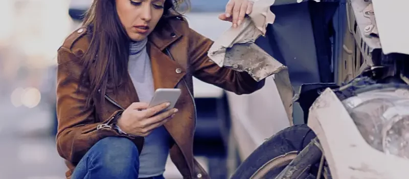 Young sad woman text messaging on smart for after a car crash on the road.