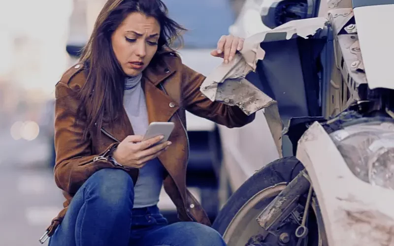 Young sad woman text messaging on smart for after a car crash on the road.