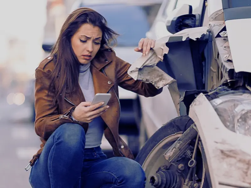 Young sad woman text messaging on smart for after a car crash on the road.