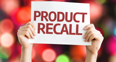 Hands holding product recall printed on a white paper with blurry lights in the background.
