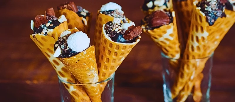 Tasty chocolate ice cream in waffle cone on brown wooden background.