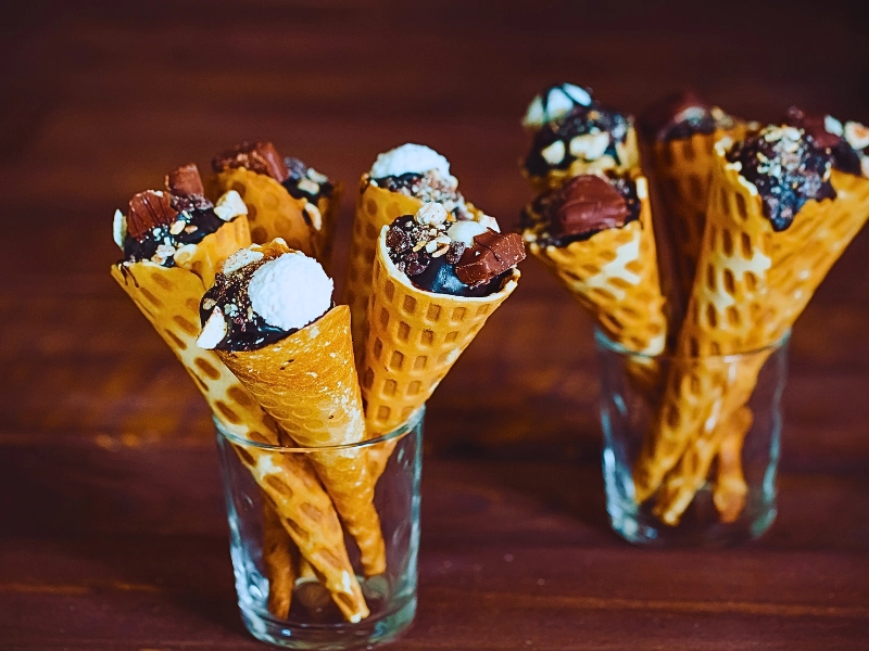 Tasty chocolate ice cream in waffle cone on brown wooden background.