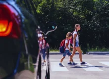 Children next to a car walking through pedestrian crossing to the school.