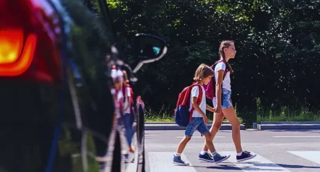 Children next to a car walking through pedestrian crossing to the school.