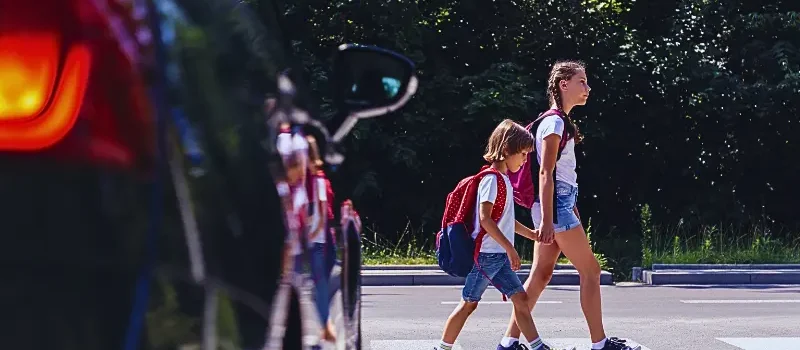 Children next to a car walking through pedestrian crossing to the school.