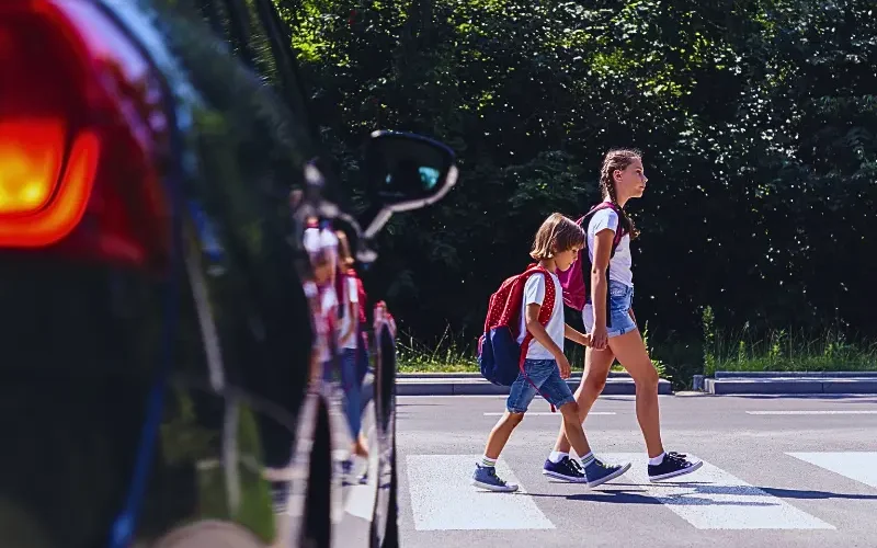 Children next to a car walking through pedestrian crossing to the school.