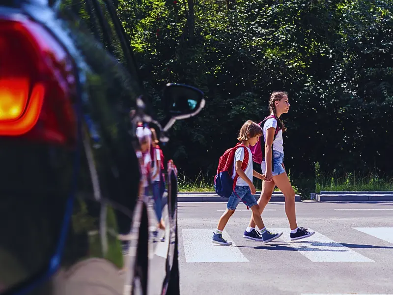 Children next to a car walking through pedestrian crossing to the school.