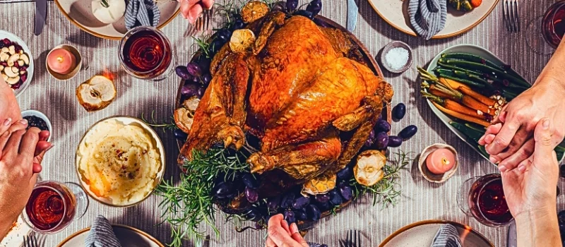 a Thanksgiving dinner scene where several people are holding hands around a table.