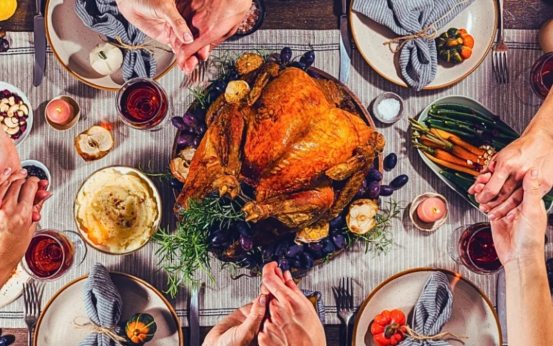 a Thanksgiving dinner scene where several people are holding hands around a table.