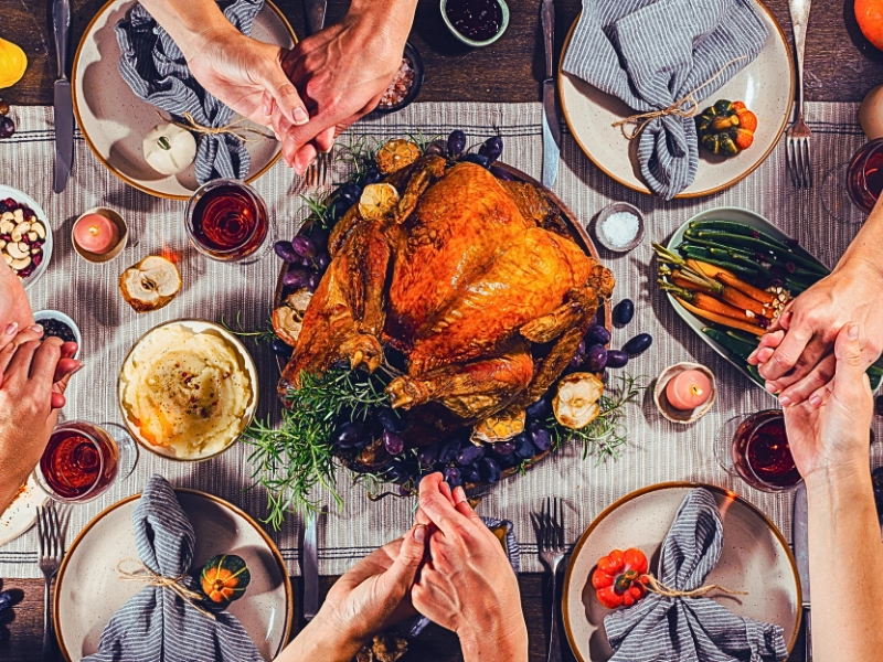 a Thanksgiving dinner scene where several people are holding hands around a table.