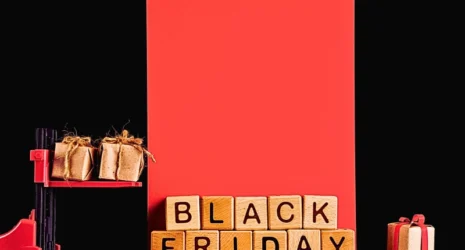 a red and black forklift carrying two small, wrapped gift boxes against a black and red background. In front of the forklift, wooden blocks spell out "BLACK FRIDAY," and a single wrapped gift box sits to the right.