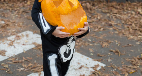 a child dressed as a skeleton carrying a pumpkin while crossing the street